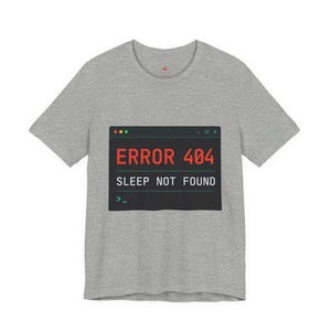Peut inclure: Un t-shirt gris chiné à manches courtes avec un motif rectangulaire noir rappelant une fenêtre de terminal informatique. Le motif affiche le texte rouge ERROR 404 et le texte blanc SLEEP NOT FOUND avec un curseur de commande vert.