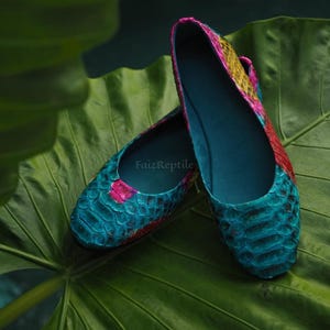 May include: A pair of flat shoes featuring a textured, scale-like pattern in vibrant shades of turquoise, yellow, and red. The interior is a solid dark blue, and the text FaizReptile is visible on the inner sole of the shoe.