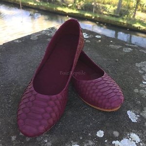 Könnte beinhalten: Ein Paar tiefburgunderrote flache Schuhe mit einem strukturierten, schuppenartigen Muster auf der Außenseite. Die Schuhe haben eine abgerundete Spitze, einen tief ausgeschnittenen Rand und ein glattes Innenfutter. Der Text "Faiz Reptile" ist sichtbar.