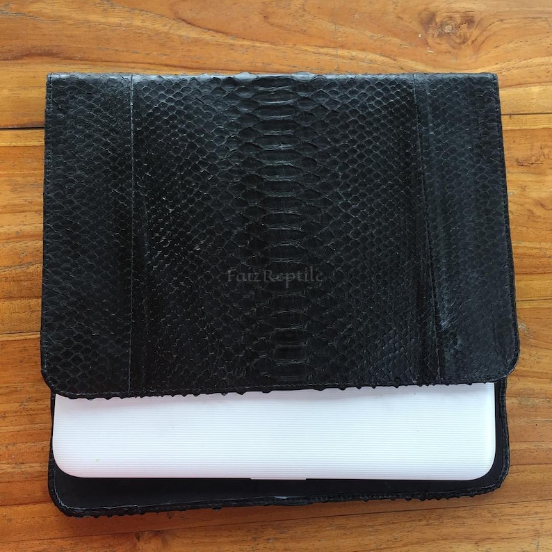 Peut inclure: Une pochette rectangulaire noire avec un motif textur&eacute; en peau de serpent et une fermeture &agrave; rabat. Le texte Farz Reptile est gaufr&eacute; sur le rabat avant. Un appareil &eacute;lectronique rectangulaire blanc est partiellement ins&eacute;r&eacute; dans la pochette.