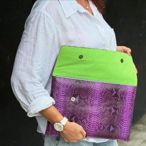 May include: A rectangular clutch bag featuring a purple snakeskin-textured exterior and a bright lime green interior flap. The bag includes two silver-toned metal snap buttons on the front and two matching snap buttons on the interior lime green lining.
