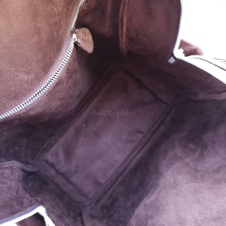 May include: The interior of a dark brown bag featuring a soft suede-like lining, a silver-toned metal zipper along the top opening, and a small leather zipper pull. The text FaizReptile is printed in the center of the dark brown interior base.