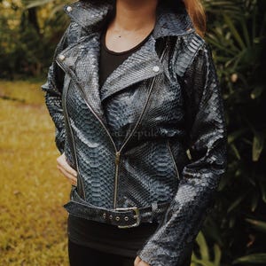 May include: A dark blue and black snakeskin-patterned motorcycle jacket featuring a wide collar, silver-tone metal snap buttons, a central zipper closure, and a matching adjustable belt with a silver-tone buckle at the waistline.