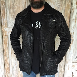 Könnte beinhalten: Eine schwarze Jacke mit strukturiertem Schlangenledermuster, ausgestattet mit einem breiten Reverskragen, einem diagonalen Frontreißverschluss und langen Ärmeln. Die Jacke wird über einem schwarzen T-Shirt mit weißem Text "Paiz Reptile" getragen.