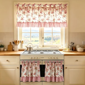 May include: A set of window and oven curtains featuring a cream background with a red floral pattern and a red and white gingham ruffle trim. The curtains are hung with red and white striped fabric ties at the top of the window and oven door.