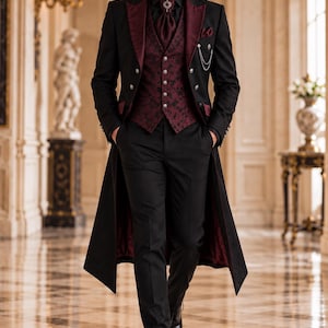Op de afbeelding: Een zwarte pandjesjas met bordeauxrode revers, een bijpassend bordeauxrood vest met patroon en zilveren knopen, een zwart overhemd, een bordeauxrode plastron met een zilveren speld, een zwarte broek en zwarte nette schoenen met een zilveren horlogeketting.