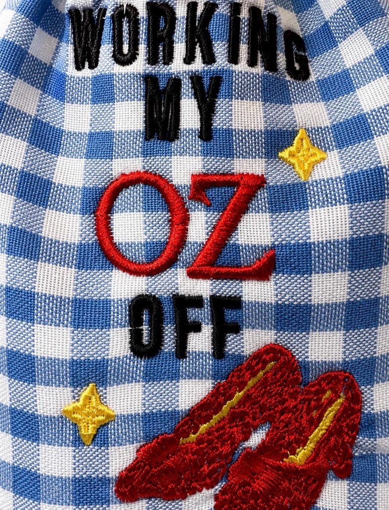 May include: A blue and white gingham fabric pouch featuring black embroidered text that reads WORKING MY OFF with the red embroidered word OZ in the center. The design includes two yellow embroidered stars and a pair of red slippers.