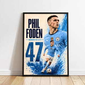Può includere: Un poster incorniciato raffigurante Phil Foden del Manchester City. Il design include un grande ritratto, una foto a figura intera del giocatore in divisa azzurra con il numero 47 ed effetti di schizzi di vernice blu su sfondo crema.