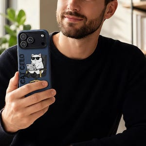 Puede incluir: Una funda de smartphone azul oscuro con una ilustración gráfica de un gato blanco con gafas de sol negras y traje, sentado en una silla de oficina mientras usa un portátil. El texto CAT CEEO está impreso verticalmente en color blanco junto al gato.