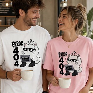 Peut inclure: Un t-shirt blanc et un t-shirt rose clair, chacun arborant un motif de chat blanc portant des lunettes de soleil et des bottes noires, assis devant un ordinateur portable. Le texte "ERROR 404" est imprimé en noir à côté du chat, avec trois points d'interrogation.