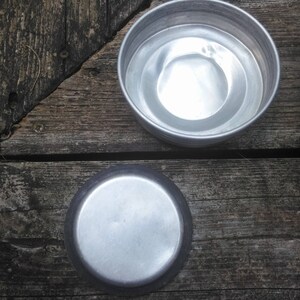 May include: Two silver metal bowls, one nested inside the other, on a wooden surface. The bowls are round and have a smooth, shiny finish.