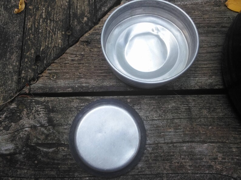 May include: Two silver metal bowls, one nested inside the other, on a wooden surface. The bowls are round and have a smooth, shiny finish.