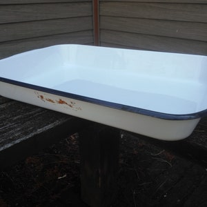 May include: White enamel baking dish with a black rim. The dish has a few brown spots on the bottom.