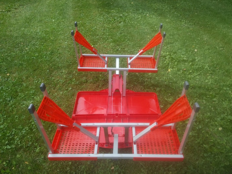 May include: A red folding table with four chairs. The table and chairs are made of metal and plastic. The table is folded up and the chairs are attached to the table.