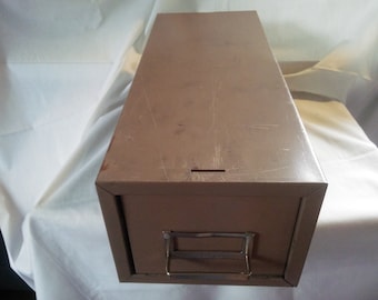 May include: A brown metal file drawer with a silver handle. The drawer is closed and has a small keyhole on the top.