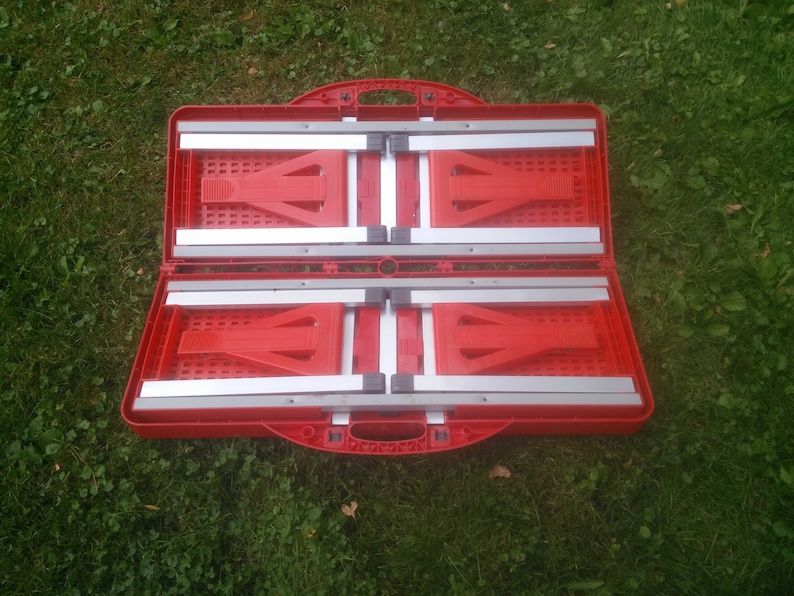 May include: Red folding table and chairs in a closed position. The table and chairs are made of red plastic with silver metal supports. The table and chairs are folded up and ready to be transported.