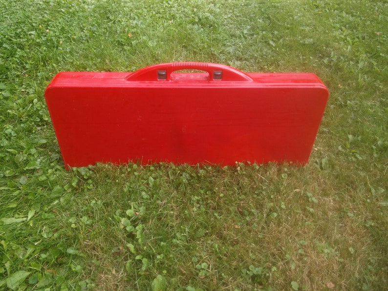 May include: A red folding table and chairs set in a closed carrying case. The case has a handle on top.