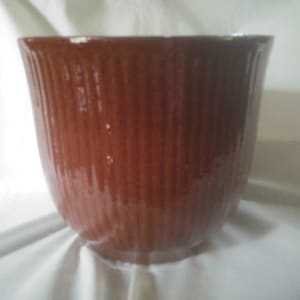 May include: A brown ceramic planter with a ribbed design. The planter is empty and has a glossy finish.