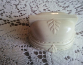 May include: A white ceramic ring box with a decorative leaf design. The box has a scalloped edge and a raised rim.