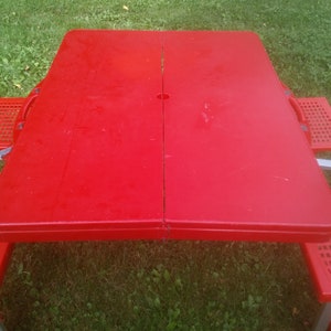 May include: Red folding picnic table with four chairs. The table has a hole in the center of the top.