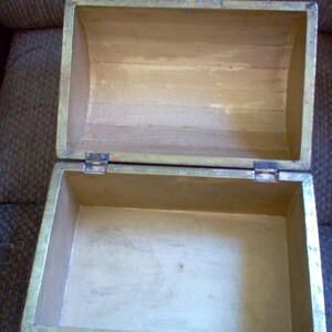 May include: An open, rectangular wooden box with a hinged lid. The box is painted gold on the exterior and has a light brown interior. The box is empty and appears to be made of wood.