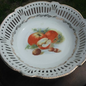 May include: White porcelain bowl with a gold rim and a cut-out design. The bowl features a painted image of apples and nuts.