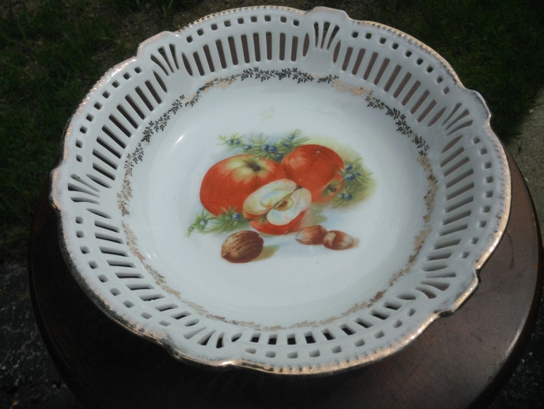May include: White porcelain bowl with a gold rim and a cut-out design. The bowl features a painted image of apples and nuts.