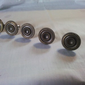 May include: Five round, silver-toned cabinet knobs with a concentric circle design and a brass-colored outer ring.