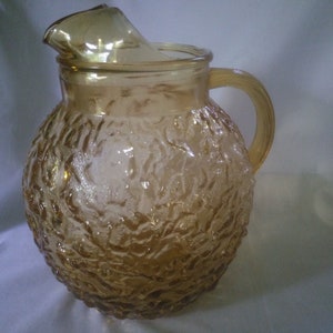 May include: A amber glass pitcher with a textured, bumpy surface. The pitcher has a round body and a handle.
