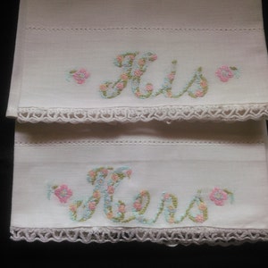 May include: Two white pillowcases with embroidered floral lettering, one says "His" and the other says "Hers".