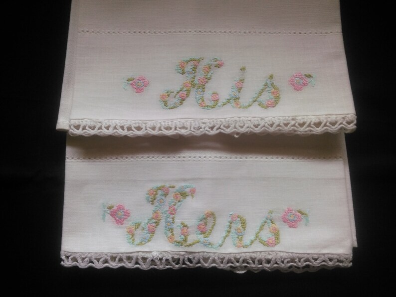 May include: Two white pillowcases with embroidered floral lettering, one says "His" and the other says "Hers".