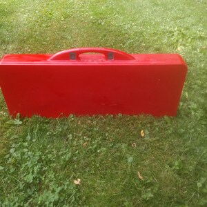 May include: A red folding table and chairs set in a closed position. The set has a carrying handle and is designed for outdoor use.