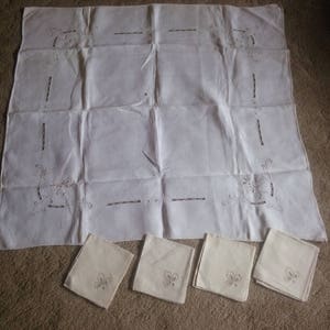 May include: A set of white linen napkins with delicate embroidered floral designs. The napkins are arranged on a white tablecloth with similar embroidery.