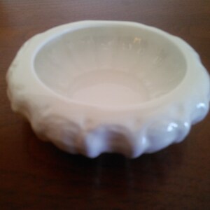 May include: A white ceramic bowl with a ruffled edge. The bowl is empty and has a smooth, glossy finish.