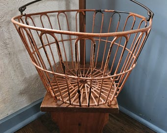 May include: A vintage orange metal basket with a wire handle. The basket is sitting on a wooden stool.