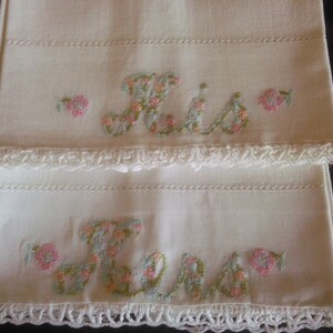 May include: Two white pillowcases with embroidered floral lettering, one says "His" and the other says "Hers".