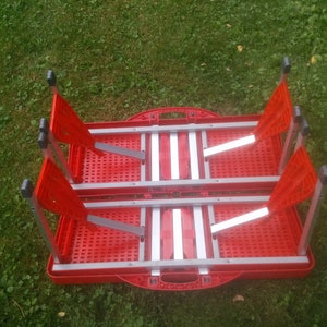 May include: Red folding table and chairs set with a silver frame. The table and chairs are folded and stacked together.