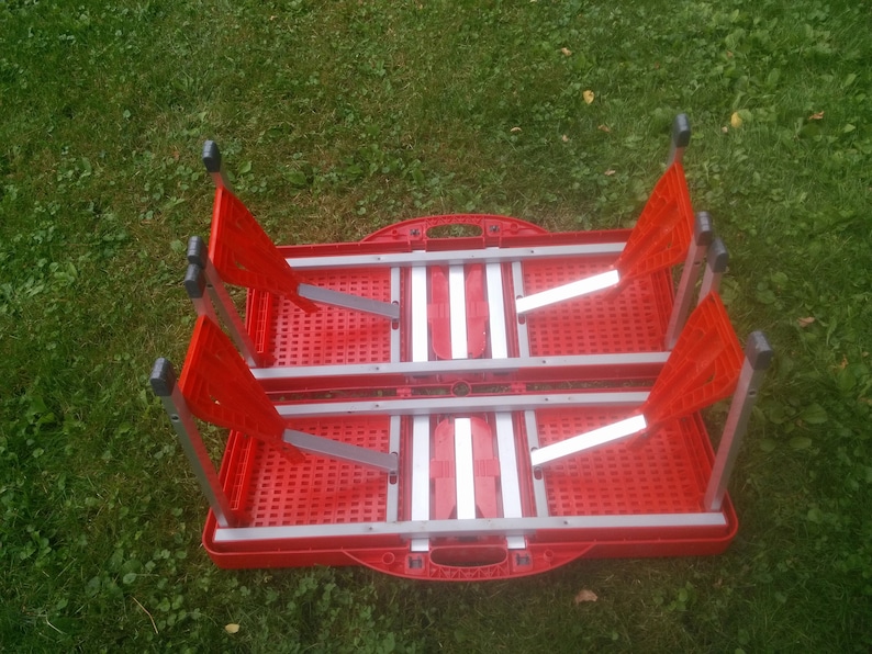 May include: Red folding table and chairs set with a silver frame. The table and chairs are folded and stacked together.