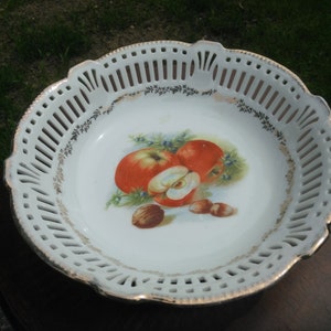 May include: White porcelain fruit bowl with a decorative gold trim and a painted design of apples and nuts. The bowl has a lacy, openwork design around the rim.