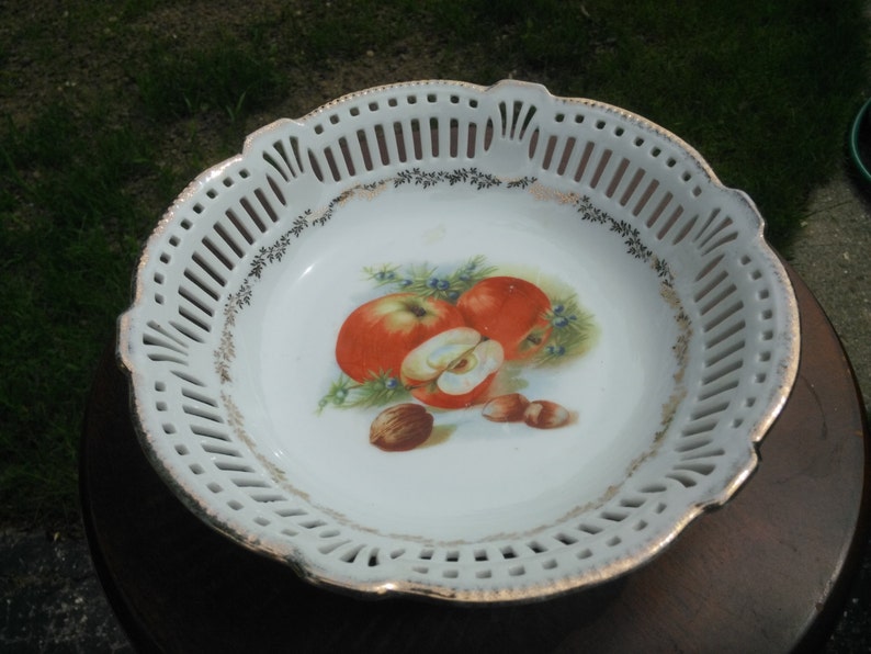 May include: White porcelain fruit bowl with a decorative gold trim and a painted design of apples and nuts. The bowl has a lacy, openwork design around the rim.
