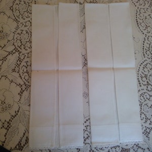 May include: Four white cotton handkerchiefs folded in half and laid out on a lace tablecloth.