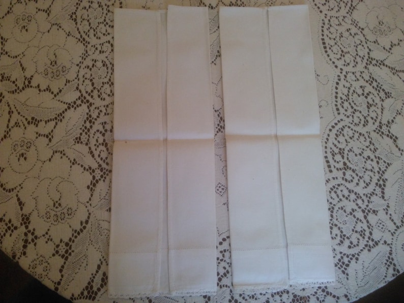 May include: Four white cotton handkerchiefs folded in half and laid out on a lace tablecloth.