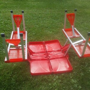 May include: A red folding picnic table with four chairs. The table is folded up and the chairs are attached to the sides. The table is made of plastic and metal.