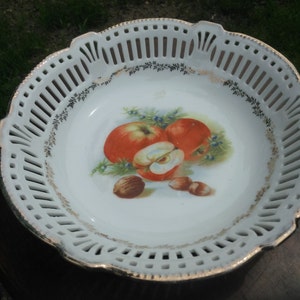 May include: White porcelain bowl with a gold rim and a cut-out design. The bowl features a painted design of apples and nuts.