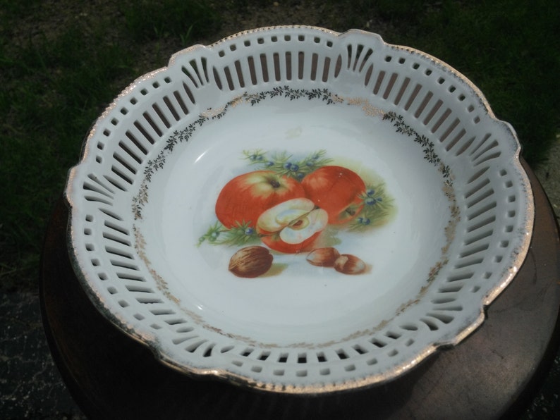 May include: White porcelain bowl with a gold rim and a cut-out design. The bowl features a painted design of apples and nuts.