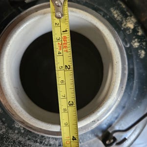 May include: Close-up of a black metal container with a white ceramic lid. A yellow measuring tape is placed next to the container, showing a measurement of 3 inches.