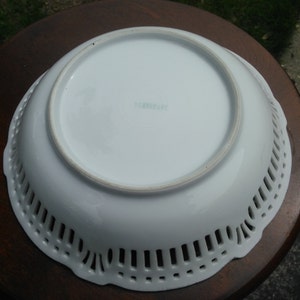May include: White porcelain bowl with a decorative openwork design around the rim. The bowl has a smooth, white interior and the words "Germany" are printed on the bottom.