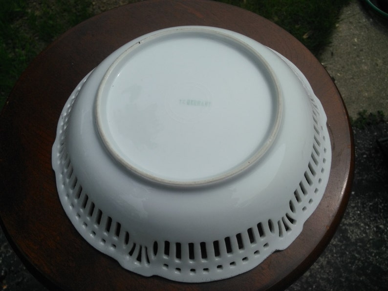 May include: White porcelain bowl with a decorative openwork design around the rim. The bowl has a smooth, white interior and the words "Germany" are printed on the bottom.