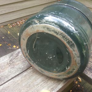 May include: The bottom of a green metal container with a worn, rusty rim. The container is round and has a slightly dented surface.
