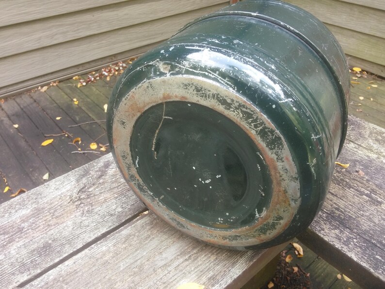May include: The bottom of a green metal container with a worn, rusty rim. The container is round and has a slightly dented surface.